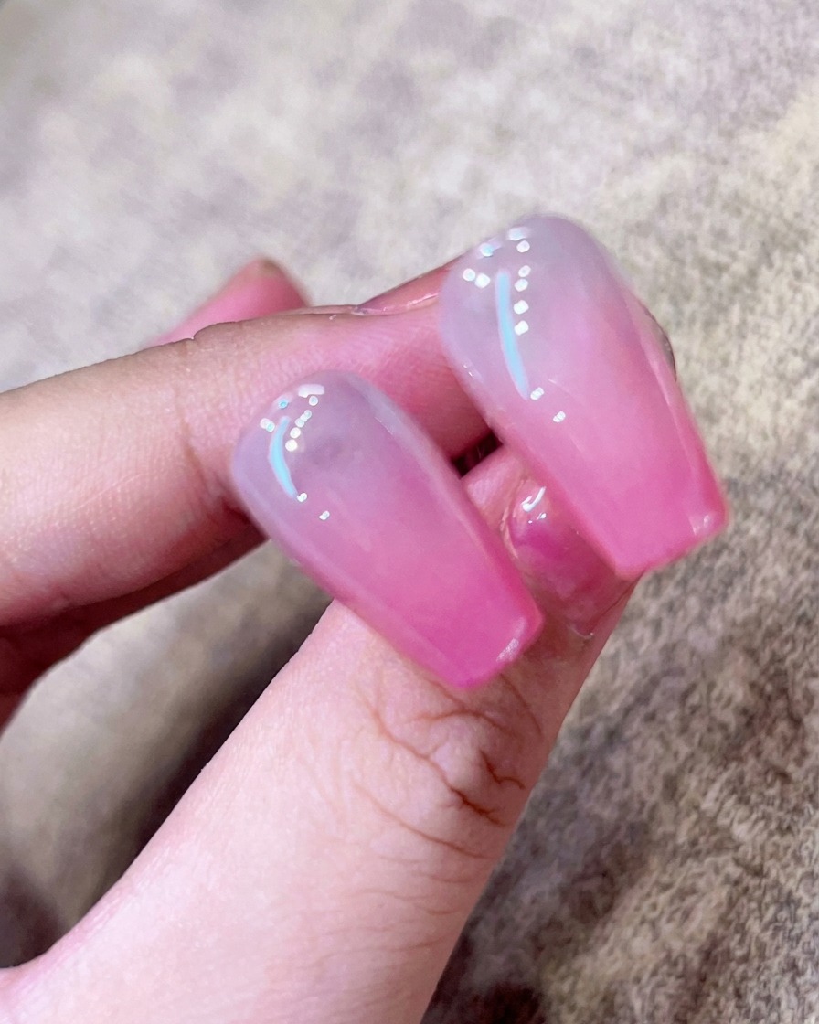 Gros plan dun pinceau appliquant un top coat transparent brillant sur un ongle ombré rose.