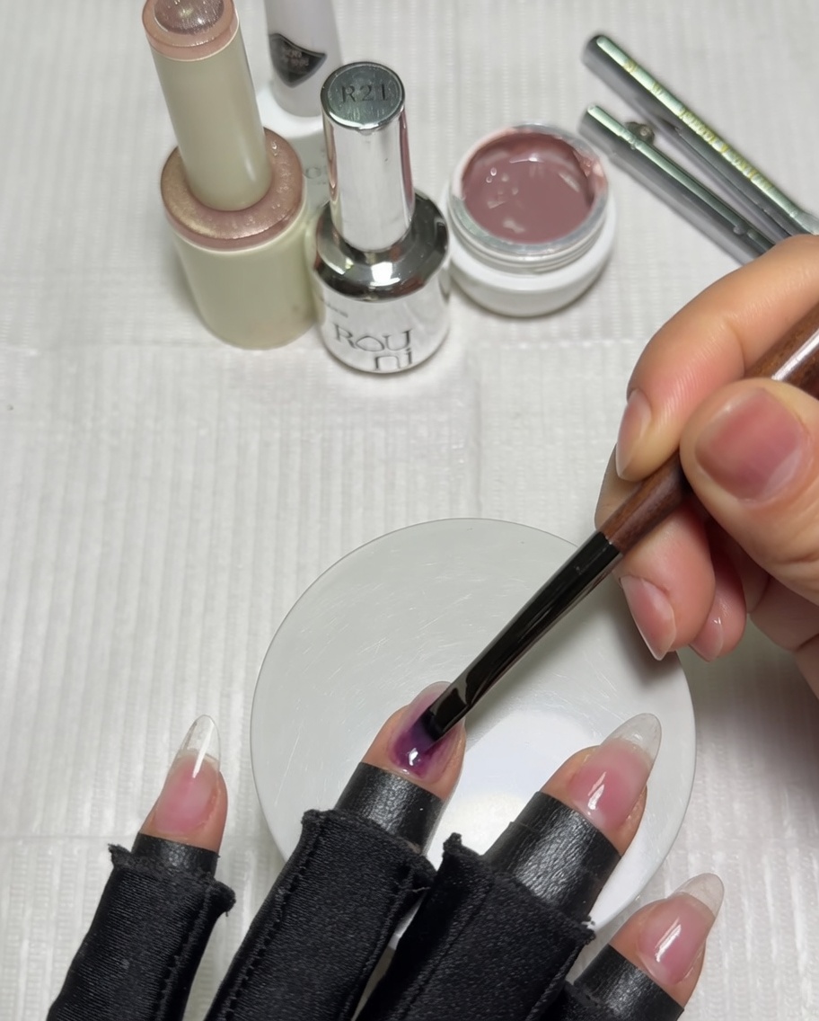 Une main positionnée dans une lampe UV violette avec une base de vernis gel nude sur les ongles.