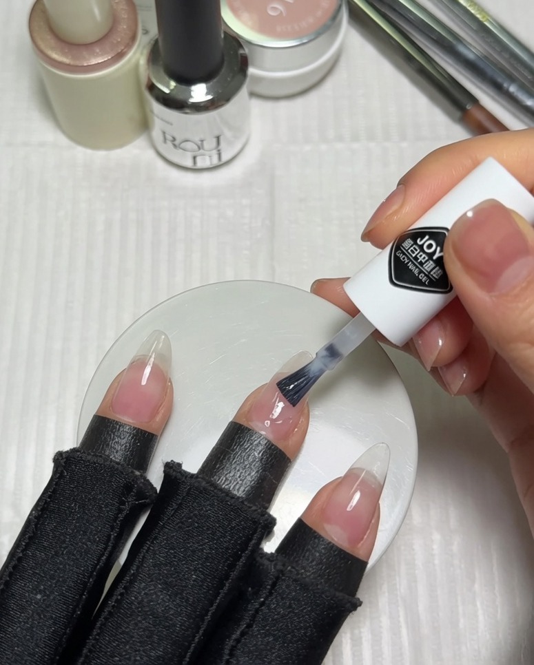 Application dun vernis gel milky white sur la moitié supérieure dun ongle nude préparé à laide du pinceau du flacon.