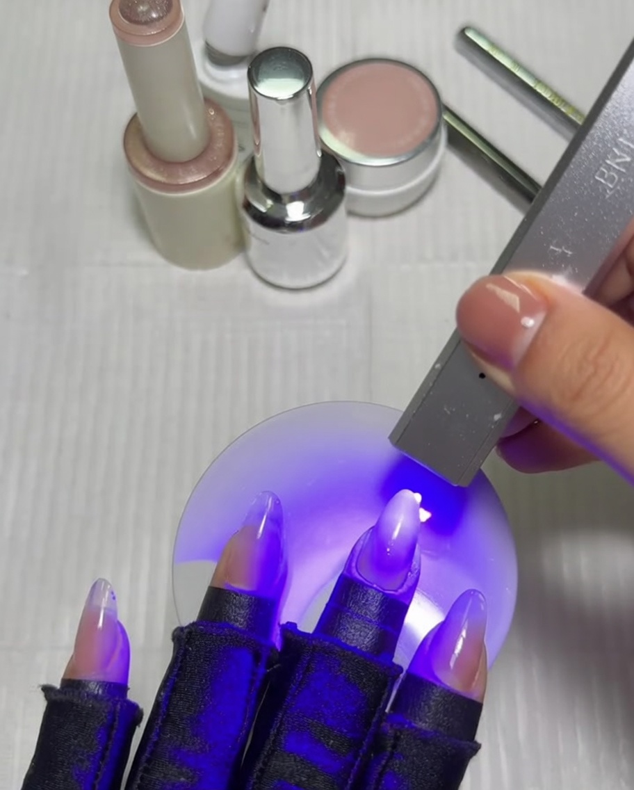 Une main avec une manucure en dégradé placée sous une lampe UV/LED, catalysant sous une lumière violette.