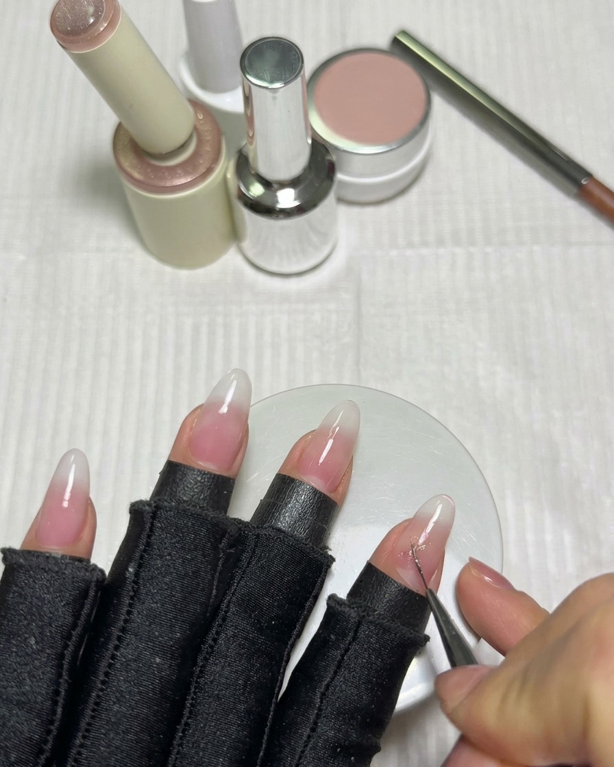 Un pinceau liner fin dessinant les lignes croisées dune étoile avec du gel cat-eye rose sur un ongle blanc laiteux.
