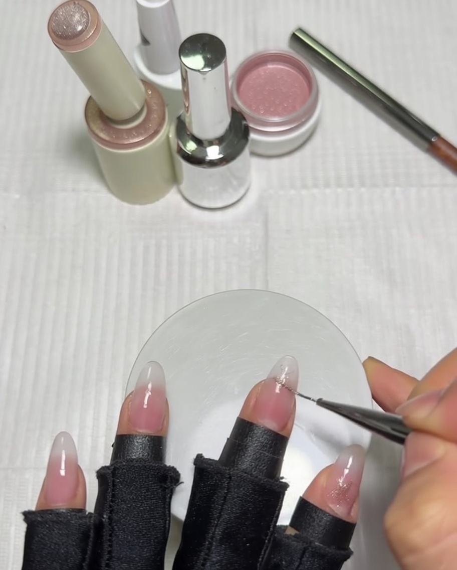 Gros plan sur une main utilisant un pinceau liner long pour détailler une étoile rose sur longle du pouce déjà doté dune base dégradée laiteuse.