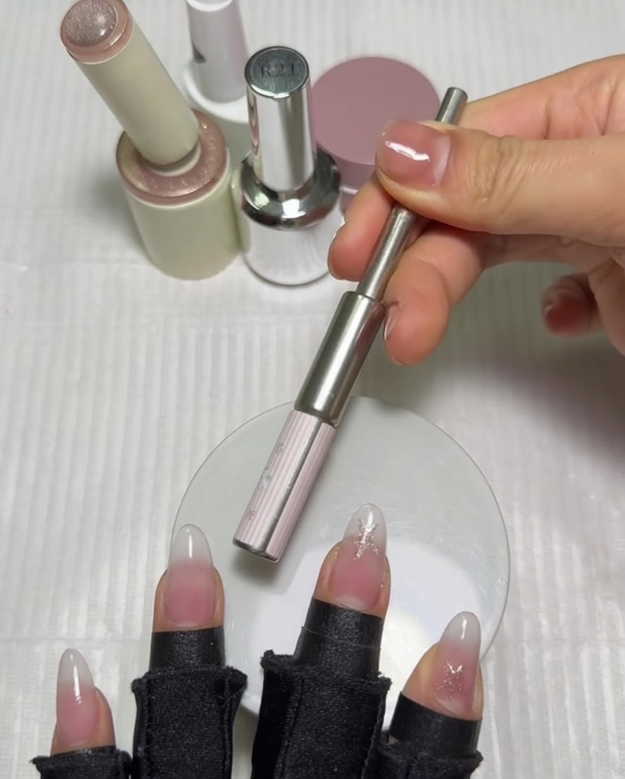 Un aimant cylindrique tenu horizontalement au-dessus de longle du pouce pour activer le vernis gel magnétique.