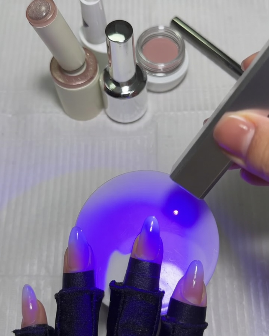 Une main avec des ongles sous une lampe UV, le pouce étant catalysé après la finition du design en étoile.