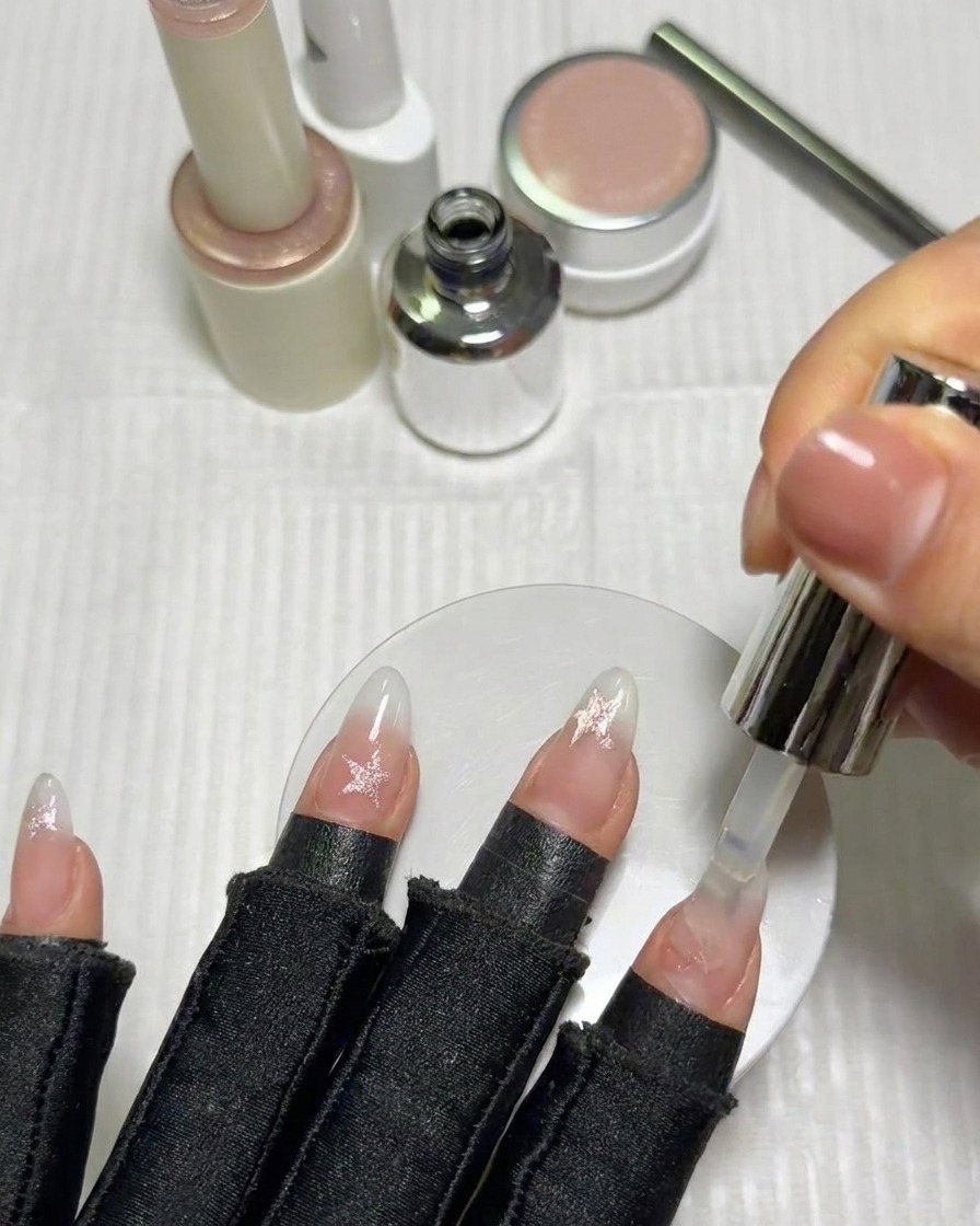 Un pinceau appliquant une couche de finition brillante sur les ongles décorés détoiles.