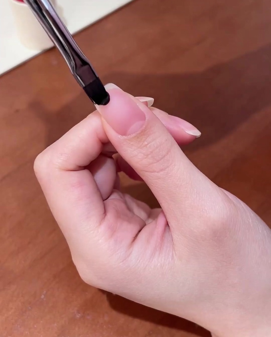 Gros plan dun pinceau appliquant une base gel transparente sur un ongle naturel propre.