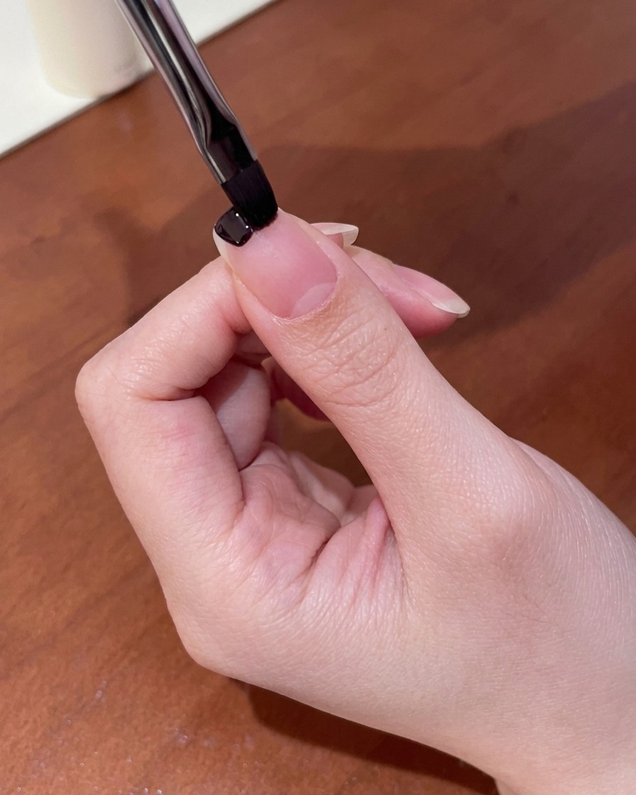 Gros plan dun petit pinceau appliquant du vernis gel violet foncé sur le bord libre dun ongle.