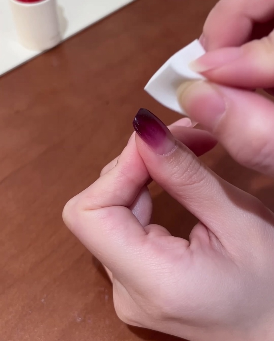 Gros plan dune main utilisant une petite éponge à maquillage blanche pour tapoter du gel violet sur un ongle afin de créer un dégradé.