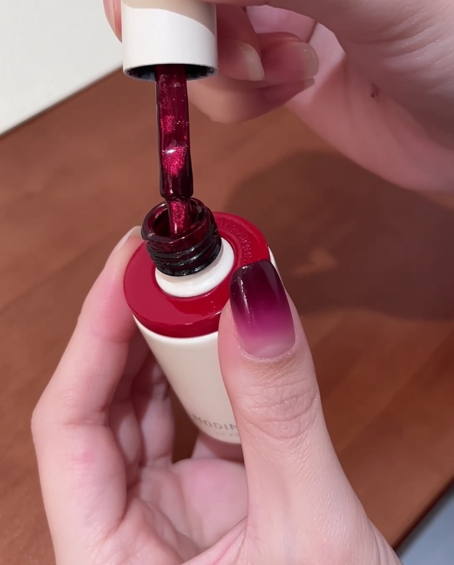 Un pinceau appliquant du vernis gel œil de chat rouge vif sur un ongle ayant déjà une base dégradée.