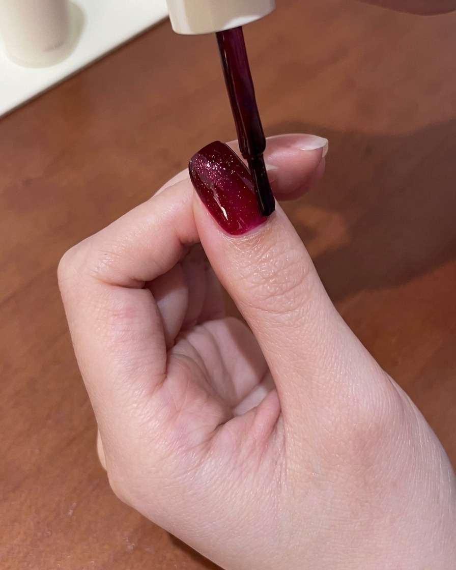 Un aimant tenu au-dessus dun ongle enduit de gel œil de chat rouge humide, attirant les reflets en une ligne brillante.