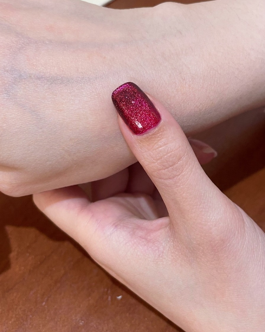 Un ongle avec le design œil de chat rouge terminé en cours de catalysation dans une lampe UV.