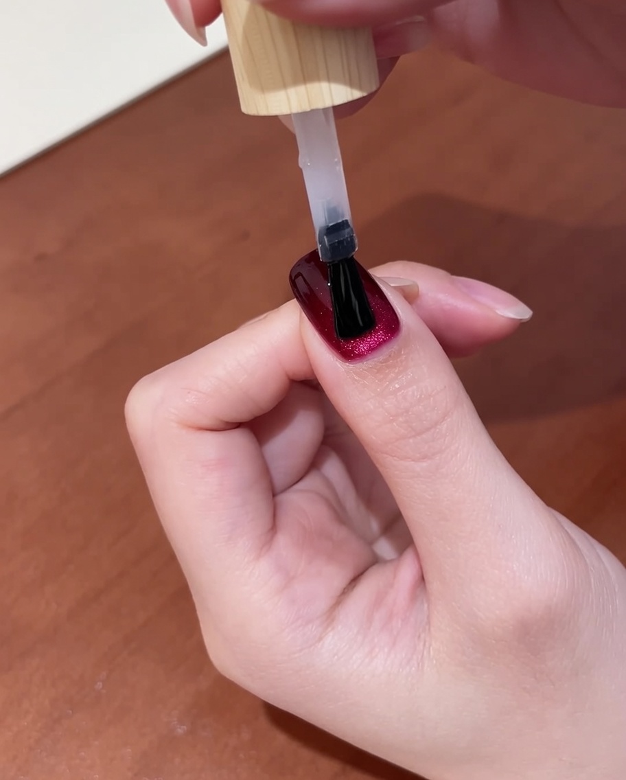 Gros plan dune main avec du top coat fraîchement appliqué sur des ongles rouge foncé œil de chat, placée dans une lampe à ongles UV pour la dernière étape de catalysation.