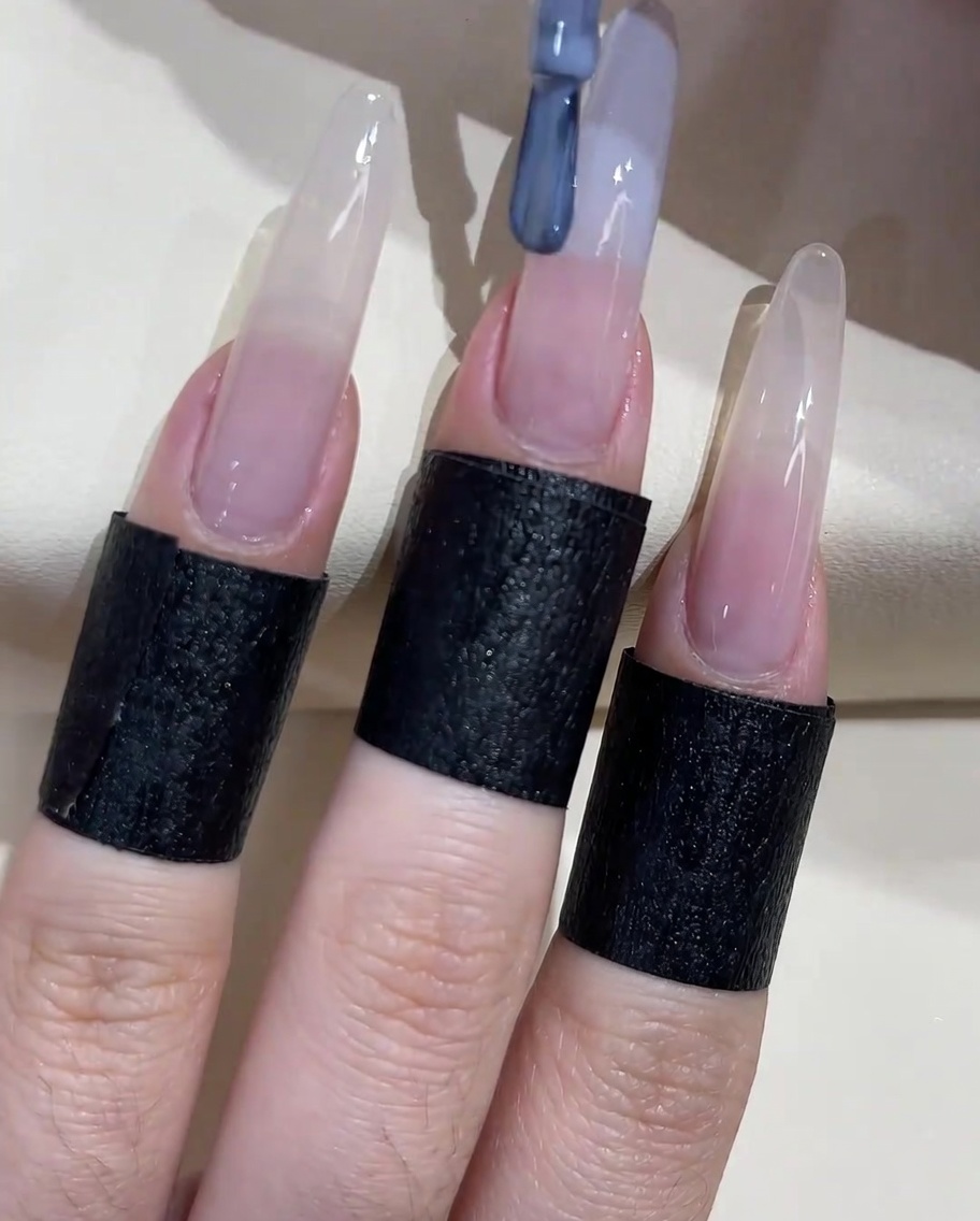 Un pinceau à ongles appliquant un vernis gel bleu-gris sur le bord libre de longle.
