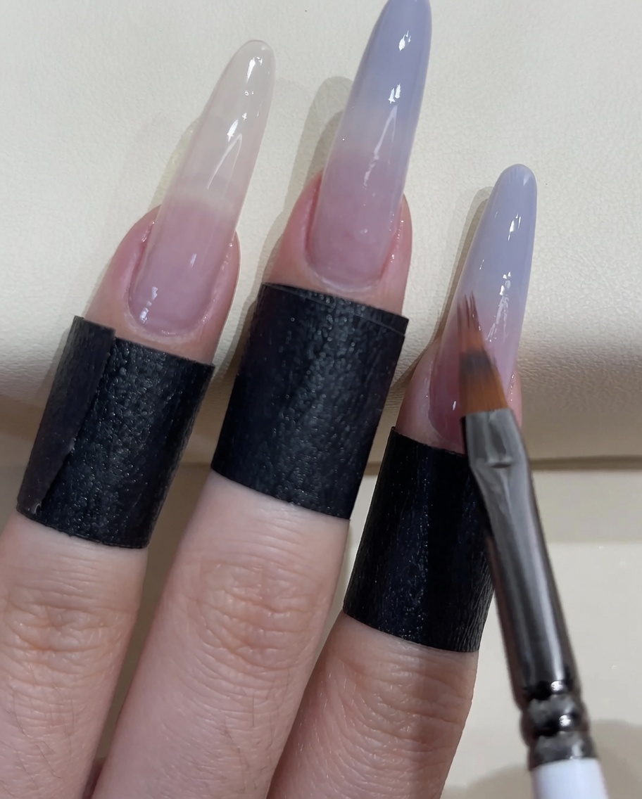 Un petit pinceau à ongles appliquant plus de vernis bleu-gris sur la pointe de longle.