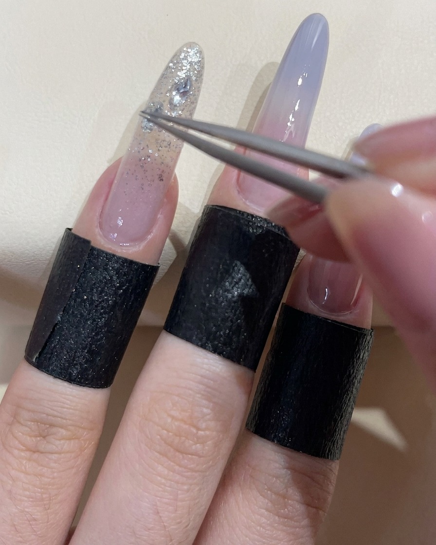 Une pince déposant un strass zircon transparent sur un ongle recouvert de gel adhésif humide.