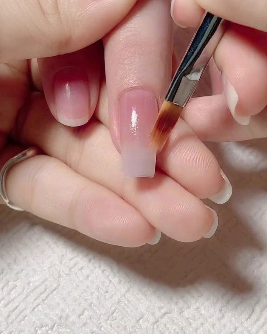 Un pinceau plat étirant doucement le gel rose jelly vers le haut pour créer un dégradé de couleur.