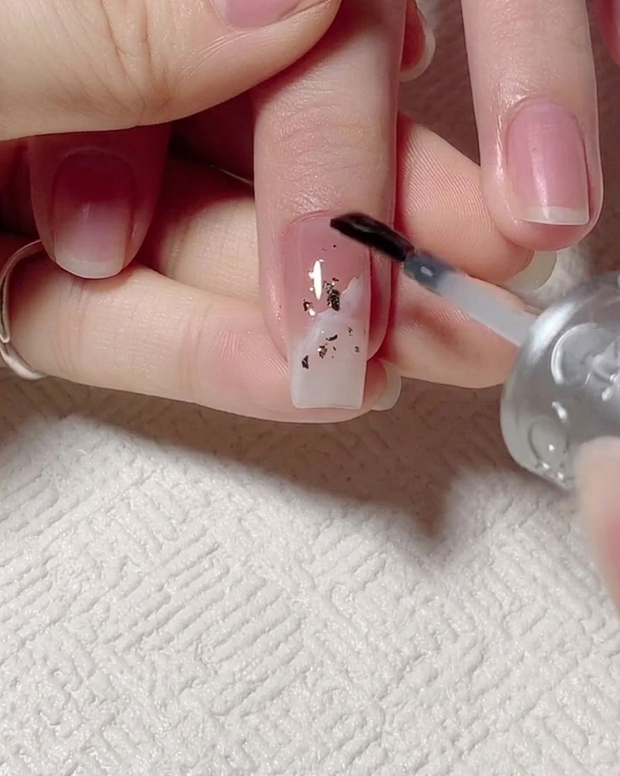 Un pinceau appliquant du gel de base transparent sur longle décoré.