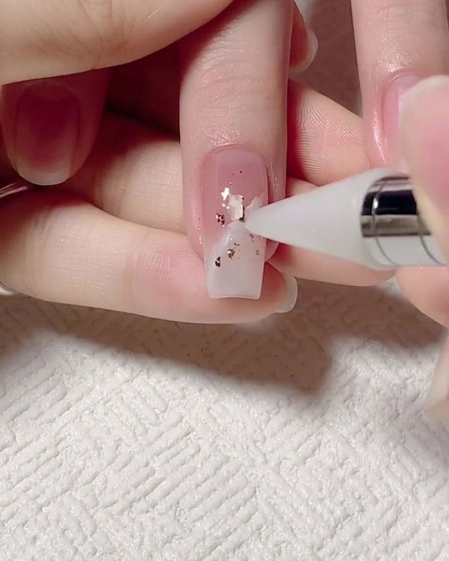 Un outil dotting plaçant de minuscules morceaux de coquillages irisés sur longle.