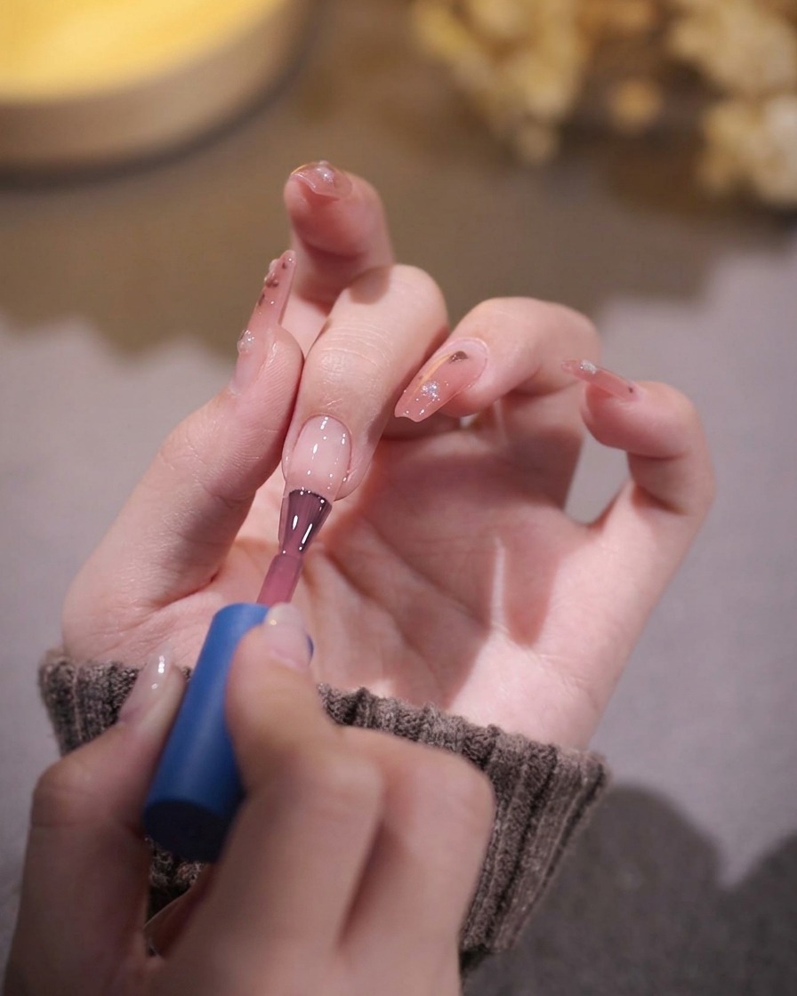 Un pinceau à ongles appliquant une couche de vernis gel rose translucide sur un ongle préparé.