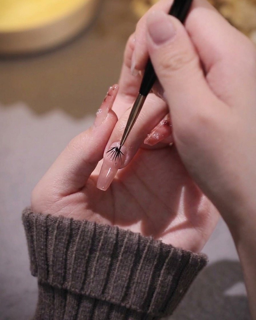 Vue rapprochée dun pinceau liner fin affinant les bords du gel rose sur un ongle.