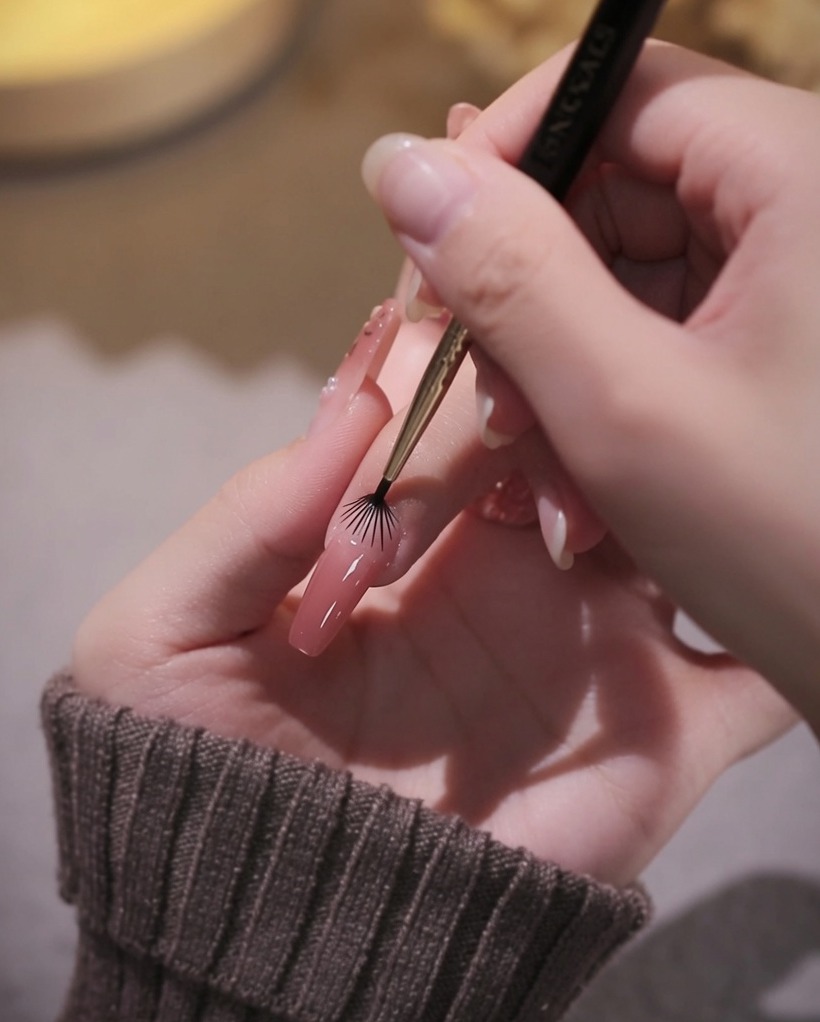 Vue rapprochée dun pinceau liner utilisé pour contourner avec précision la zone de la cuticule avec du vernis gel rose.