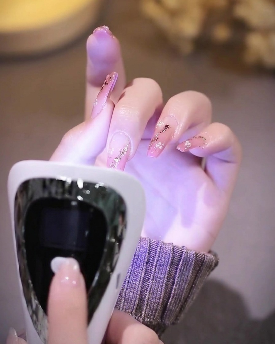 Une main aux ongles finis reposant dans une lampe à ongles UV dont lintérieur brille dune lumière violette.