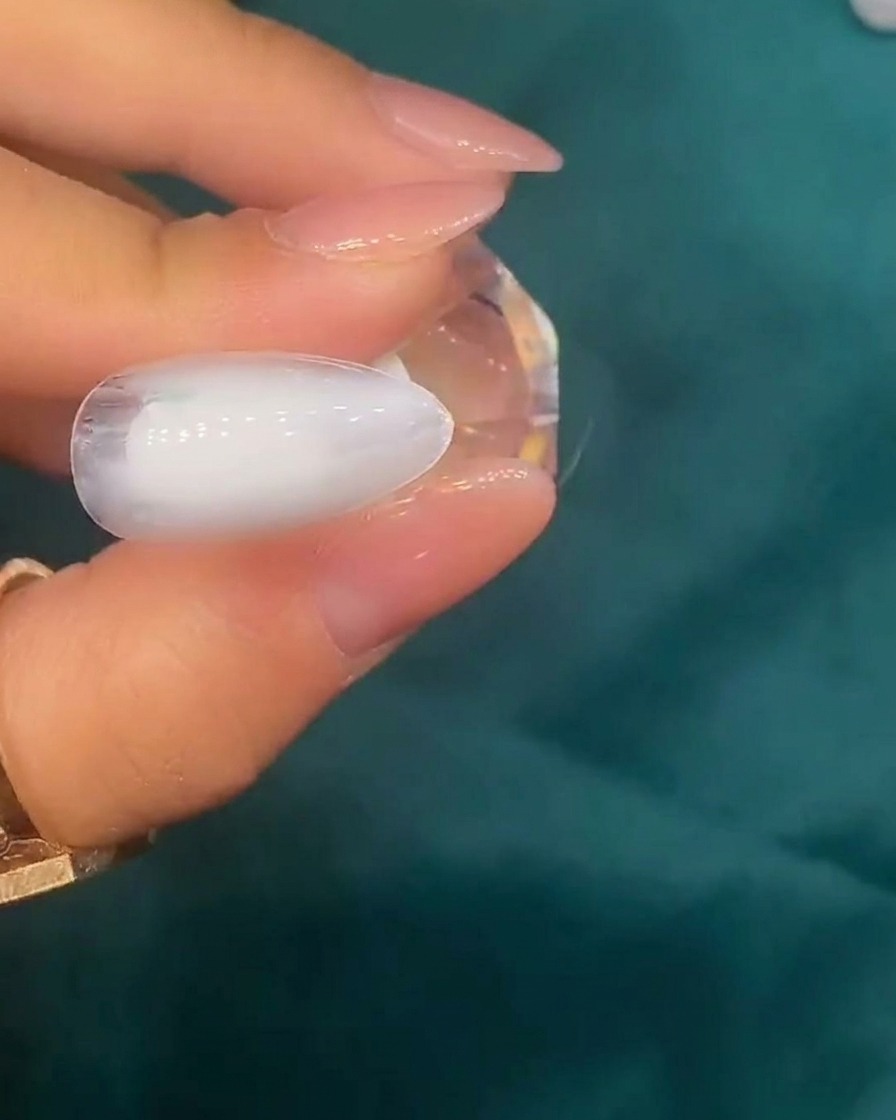 Une pince déposant de petits morceaux de coquillages irisés sur la surface dun ongle à base blanche.