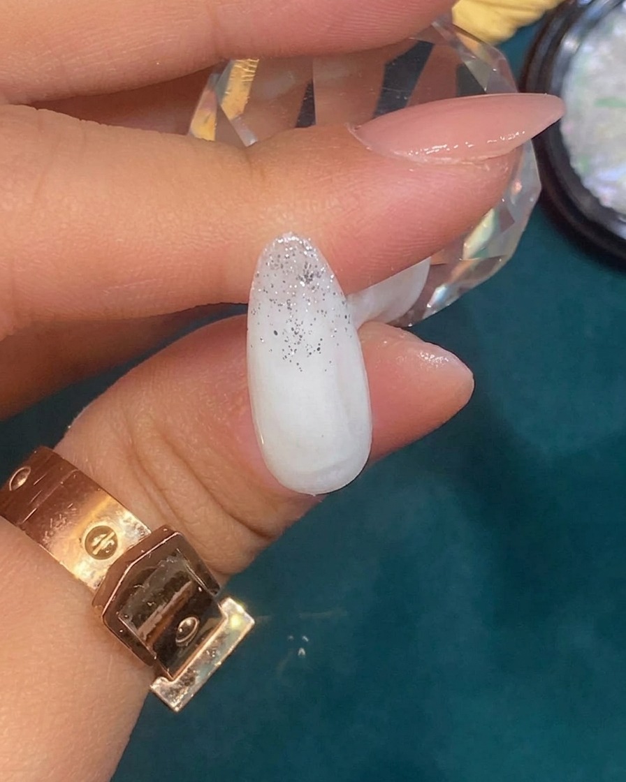 Une pince déposant un petit morceau irrégulier de feuille argentée sur un ongle avec un dégradé de paillettes.