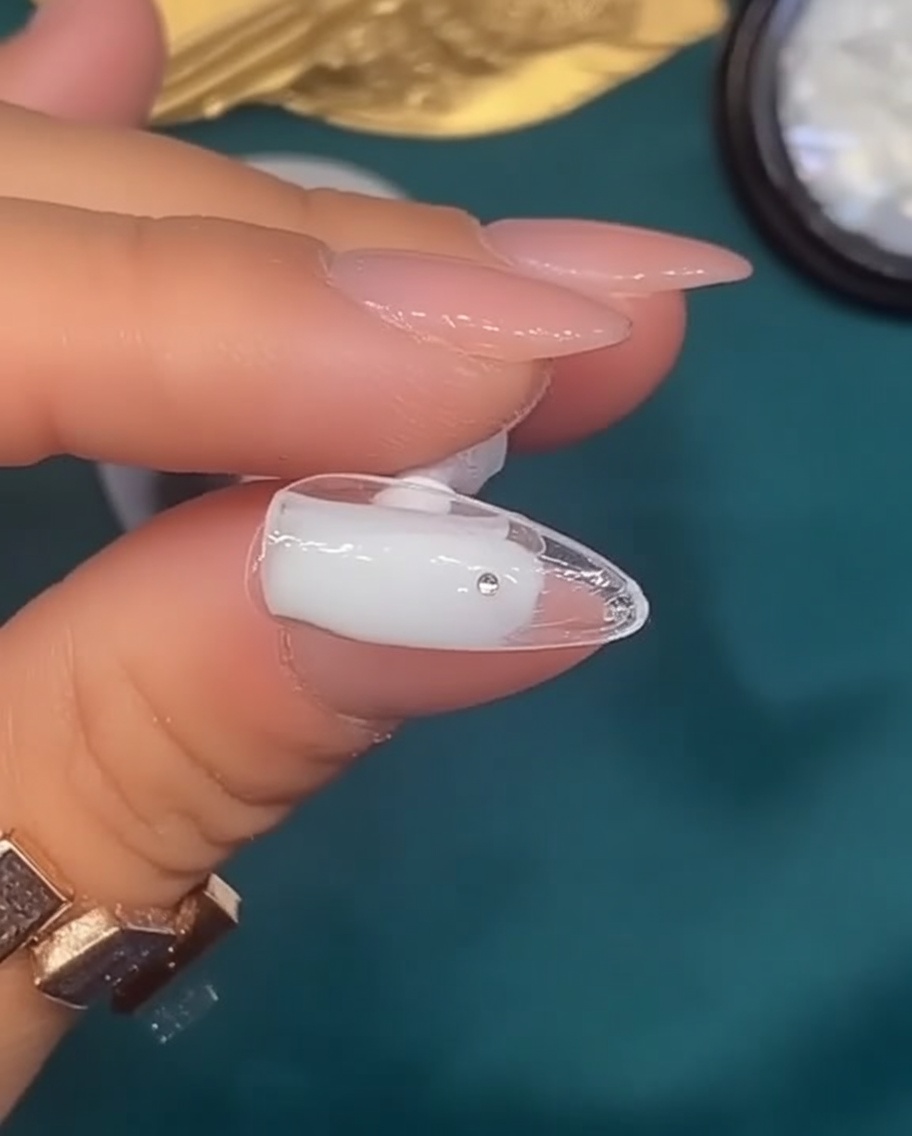 Un pinceau appliquant un vernis gel blanc laiteux translucide sur un ongle naturel.