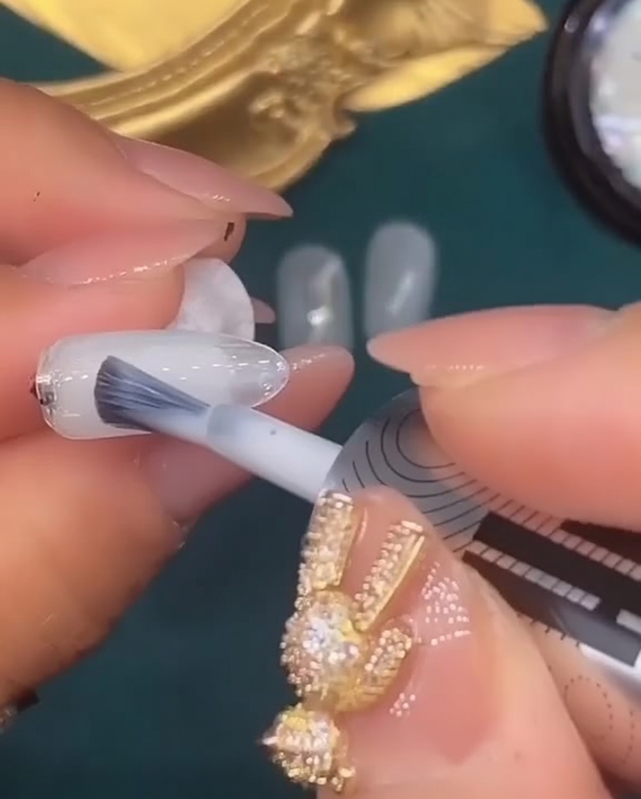 Un pinceau à ongles appliquant une couche de gel blanc translucide sur le cinquième ongle.