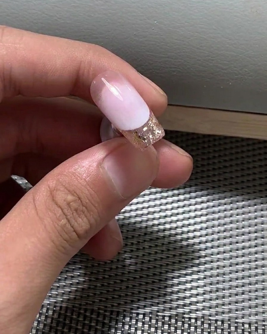 Gros plan dun pinceau appliquant une fine couche de vernis gel nude sur un ongle.