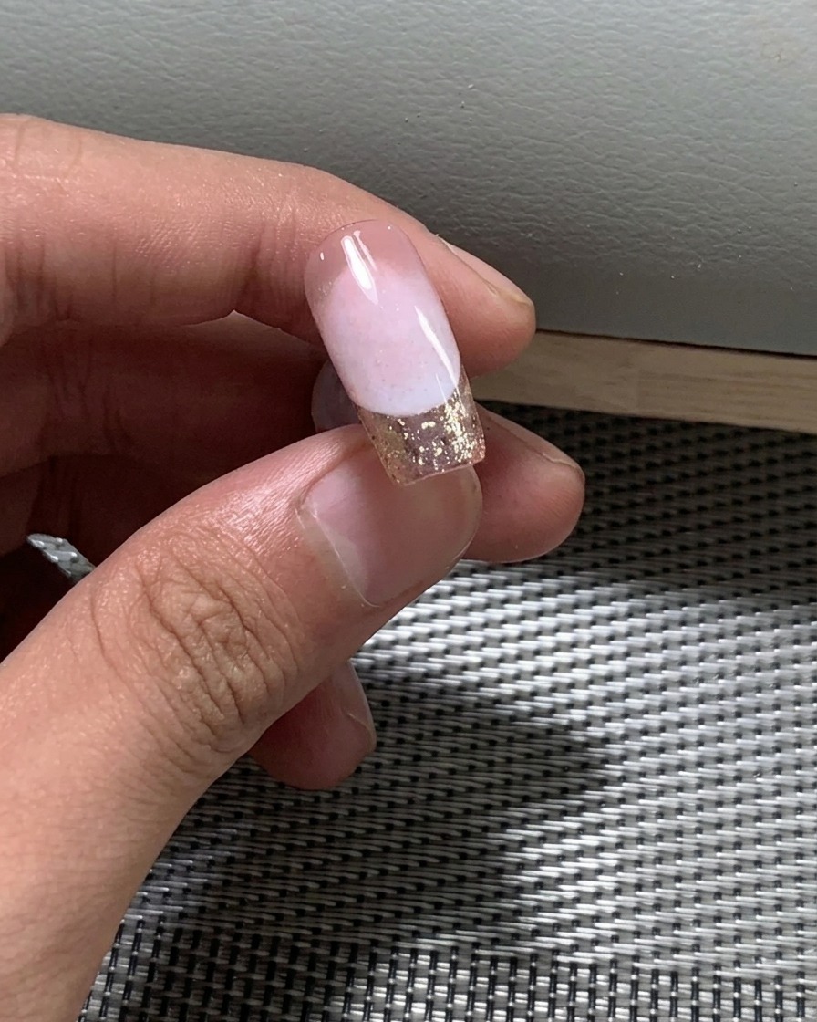 Gros plan dun pinceau appliquant une deuxième couche de vernis gel nude sur un ongle.