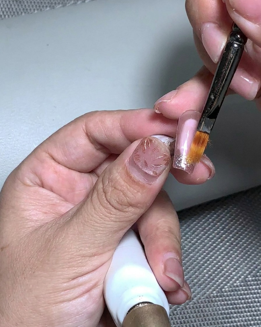 Un pinceau appliquant du gel de structure transparent sur la surface texturée de la feuille dor et des paillettes.