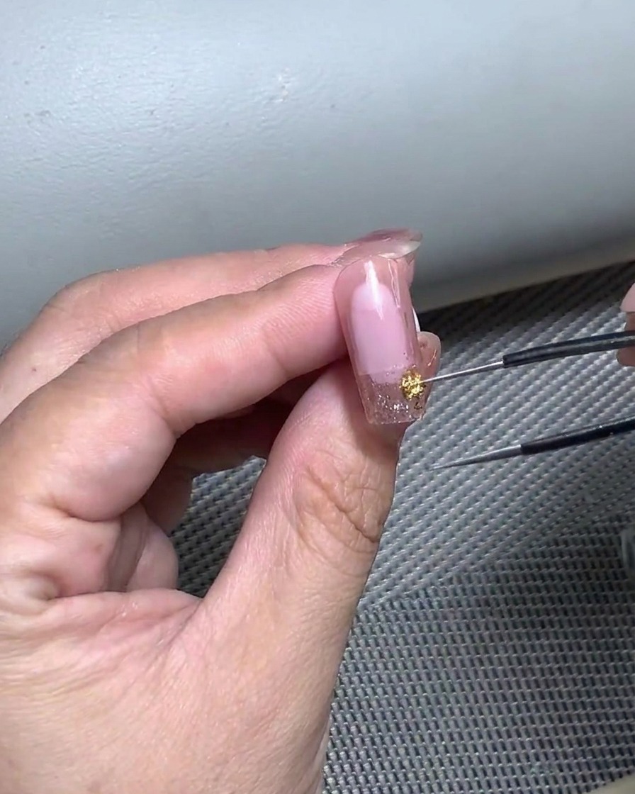 Gros plan dune main utilisant une pince pour placer délicatement un autocollant de French sur un ongle préparé au gel.