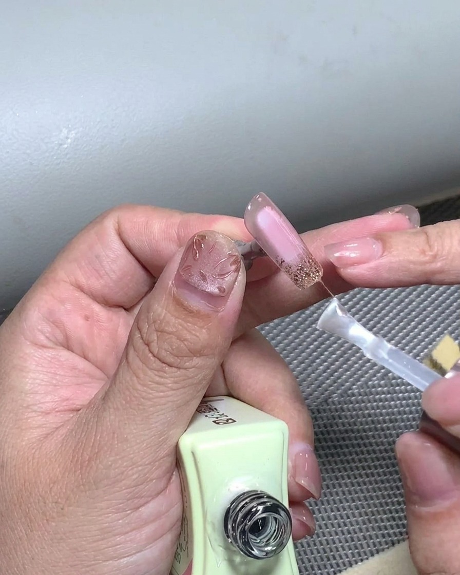 Un pinceau appliquant une couche finale de top coat transparent sur un design de French manucure terminé.