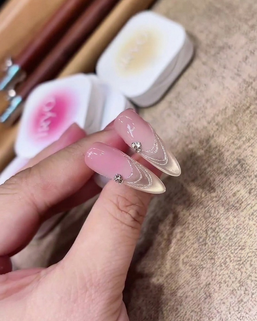 Gros plan dun pinceau gel plat appliquant uniformément un gel nude rosé transparent sur une extension dongle transparente en amande.