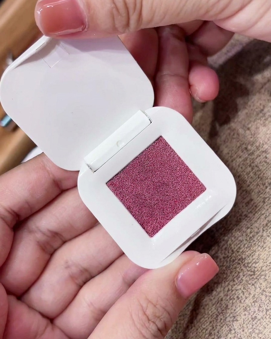 Gros plan dune éponge de maquillage triangulaire pressée dans un boîtier carré de pigment rose-violet fin.