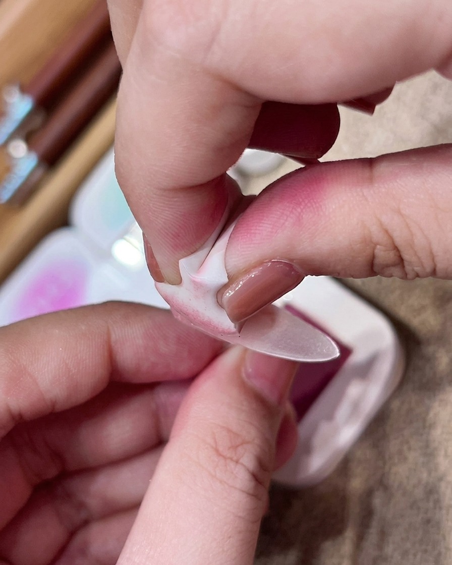 Une main utilisant une petite éponge de maquillage pour tapoter délicatement du pigment rose sur le centre dun ongle nude mat.
