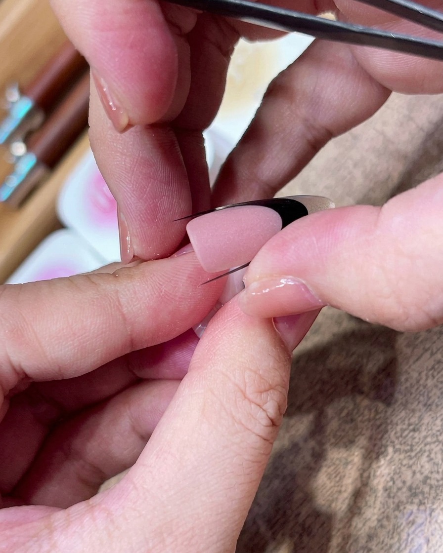 Une pince positionnant soigneusement un guide autocollant incurvé noir en diagonale sur un ongle au fini mat.