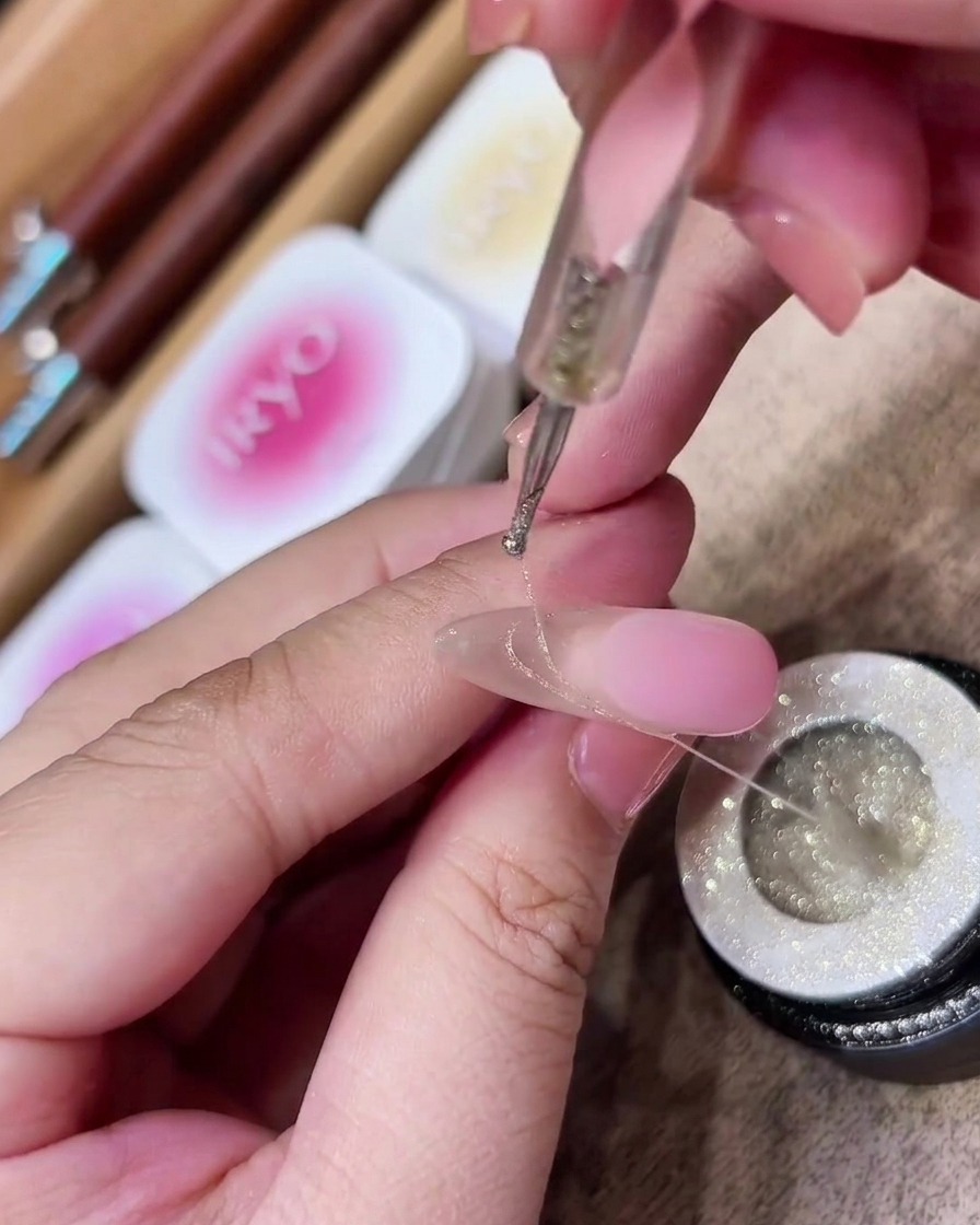 De fines lignes délicates de spider gel argenté drapées en courbes artistiques sur un ongle manucuré.