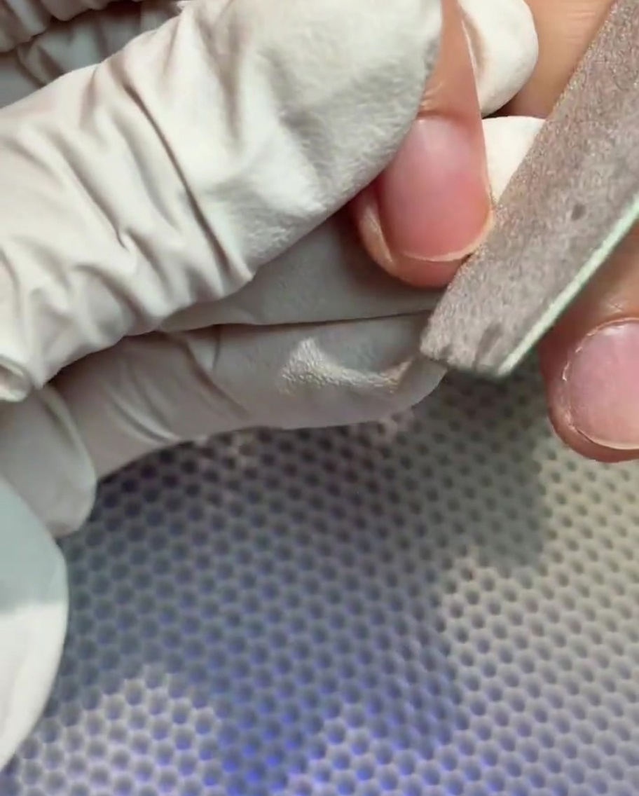 Une main gantée utilisant une lime à ongles pour façonner le bord libre dun ongle naturel.