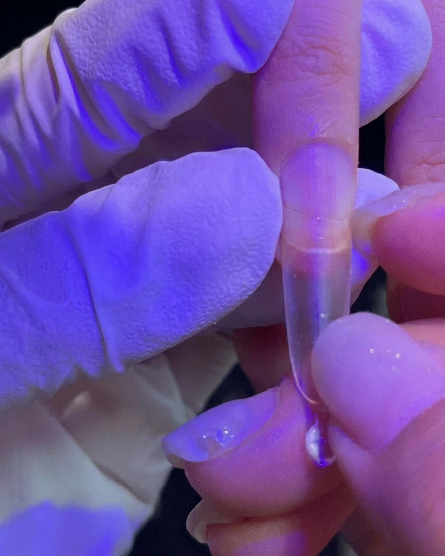 Une main pressant une capsule dextension transparente sur un ongle naturel.