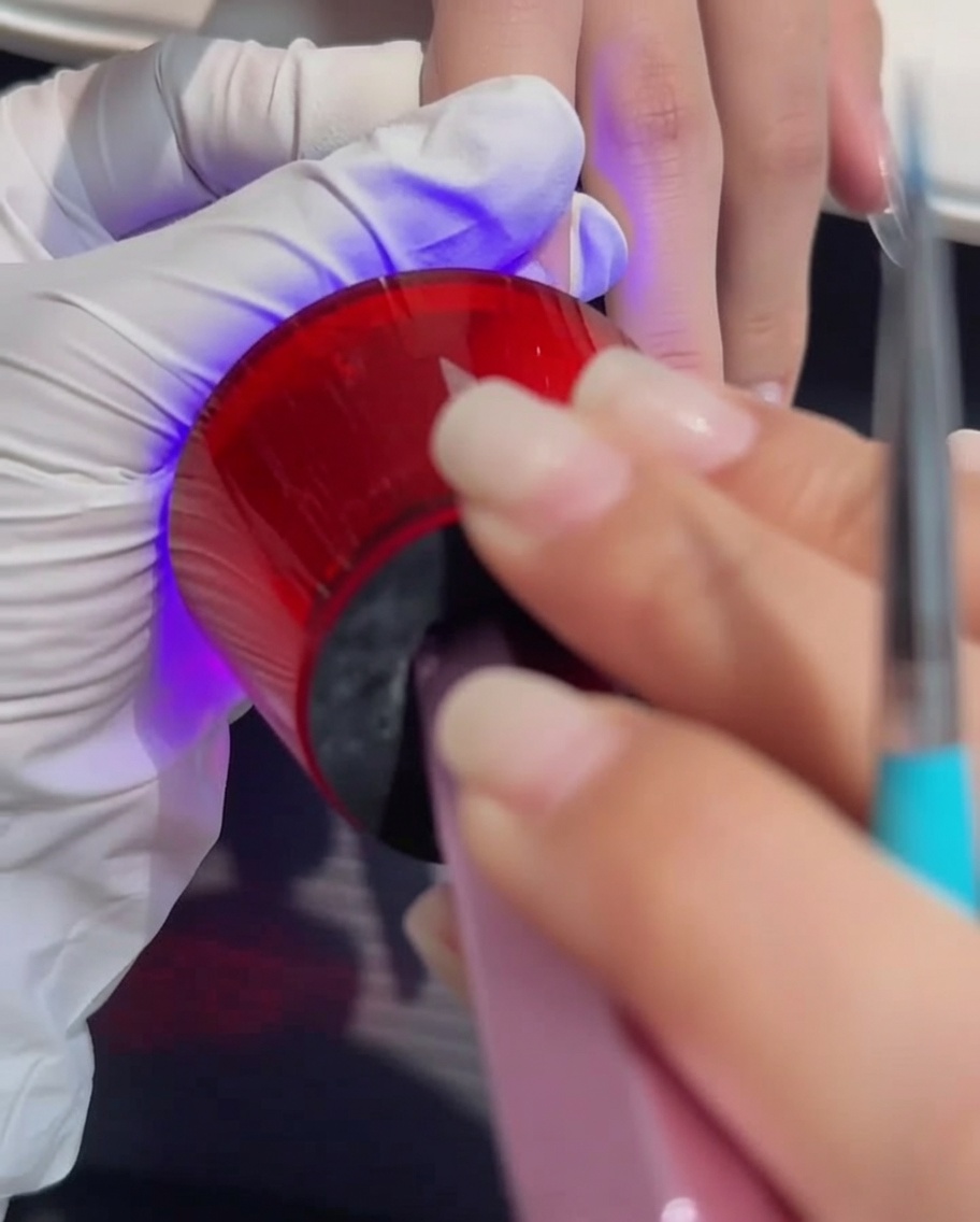 Une main placée sous une lampe UV/LED professionnelle pendant le processus de séchage.