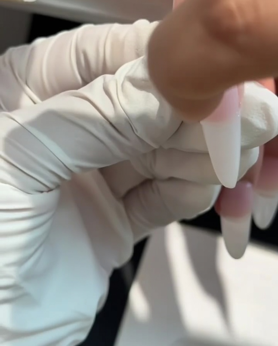 Une éponge à maquillage utilisée pour tapoter du gel blanc laiteux sur la pointe de longle.