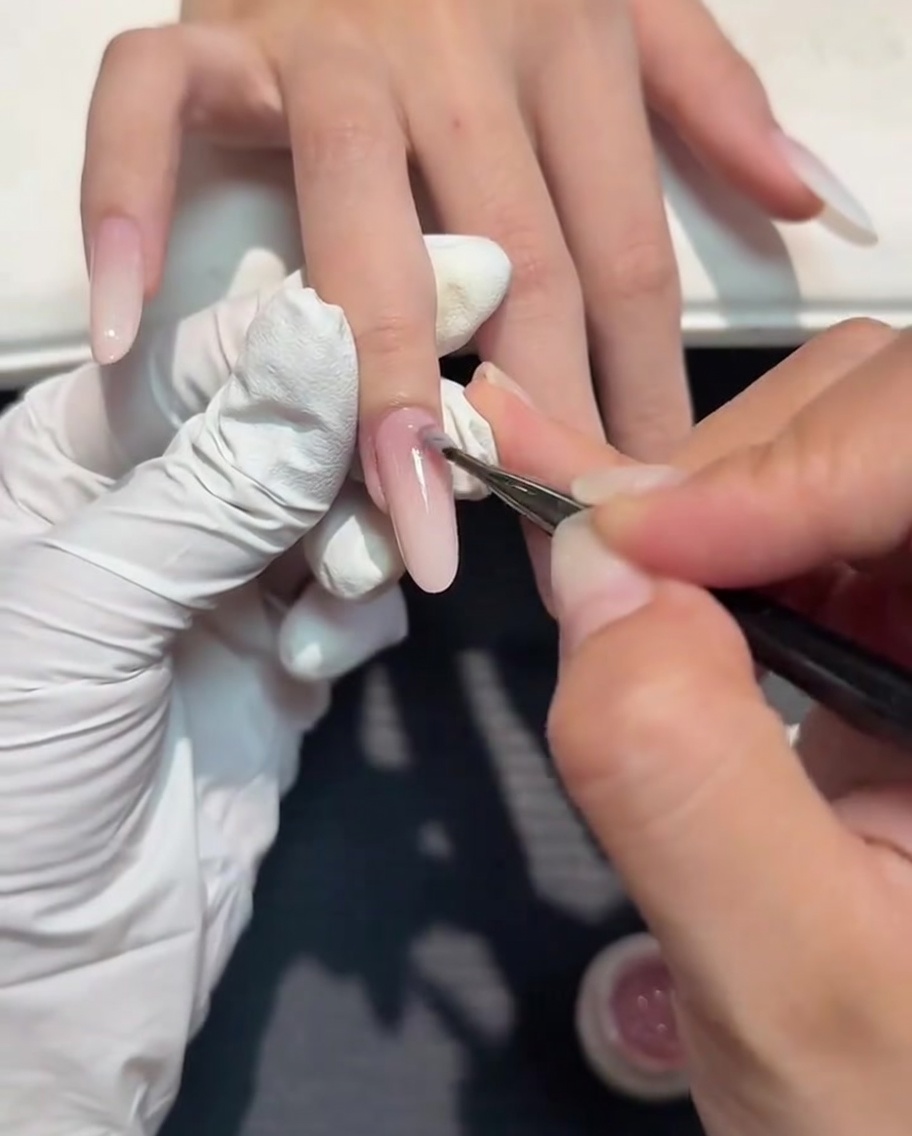 Un pinceau fin appliquant une couche de gel nude sur un dégradé blanc.