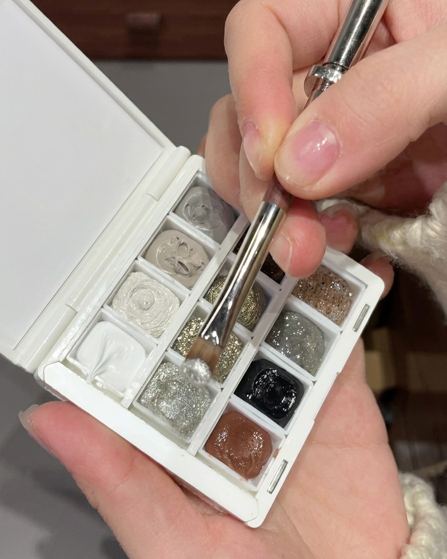 Un pinceau mélangeant du gel à paillettes argentées fines avec des sequins argentés plus gros sur une palette nail art blanche.