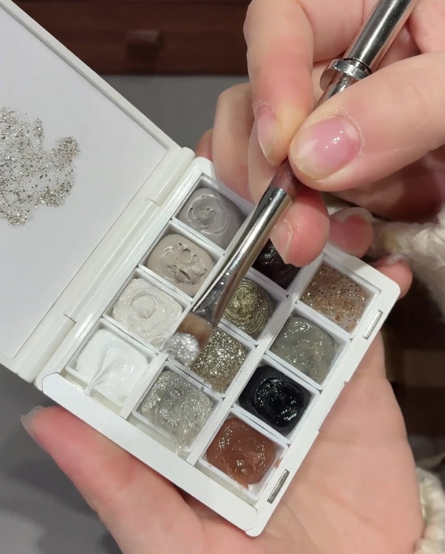 Un pinceau à ongles appliquant un mélange de paillettes et de sequins argentés à la base dun ongle naturel.