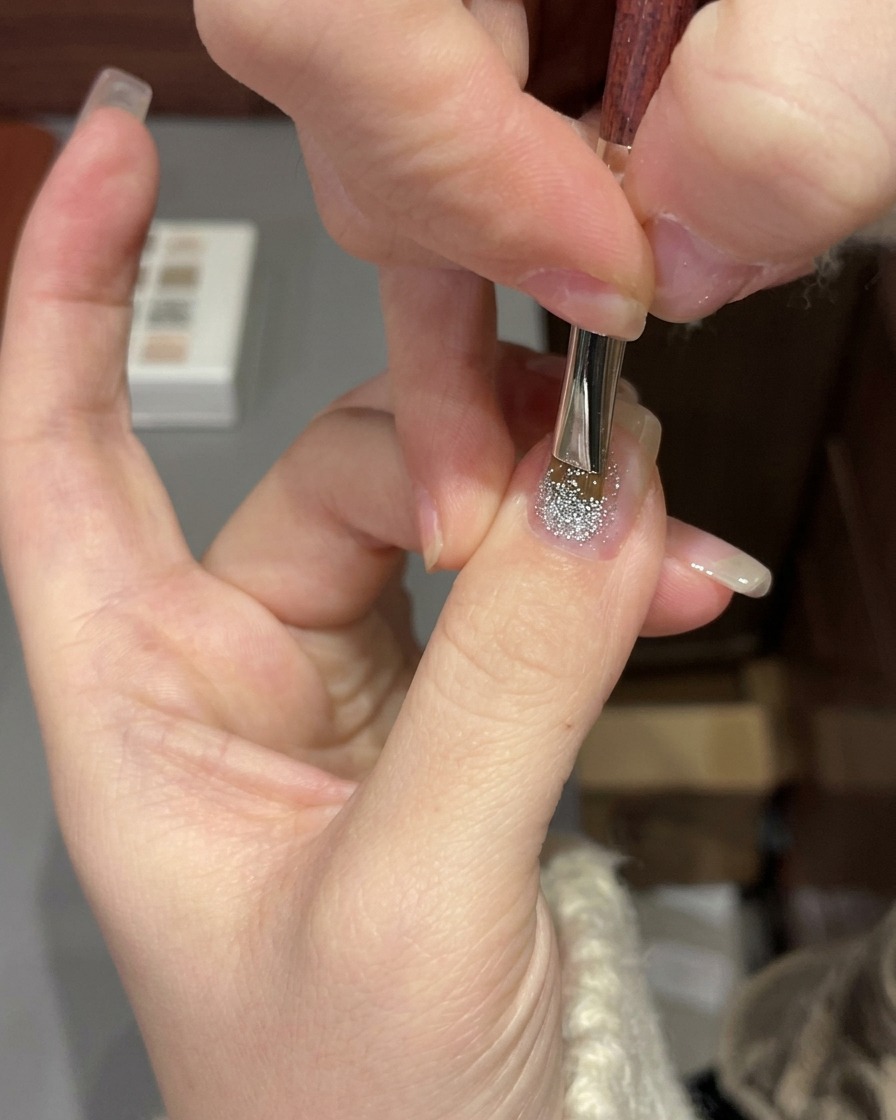 Une main placée sous une lampe UV/LED professionnelle pour catalyser une manucure en gel à paillettes.