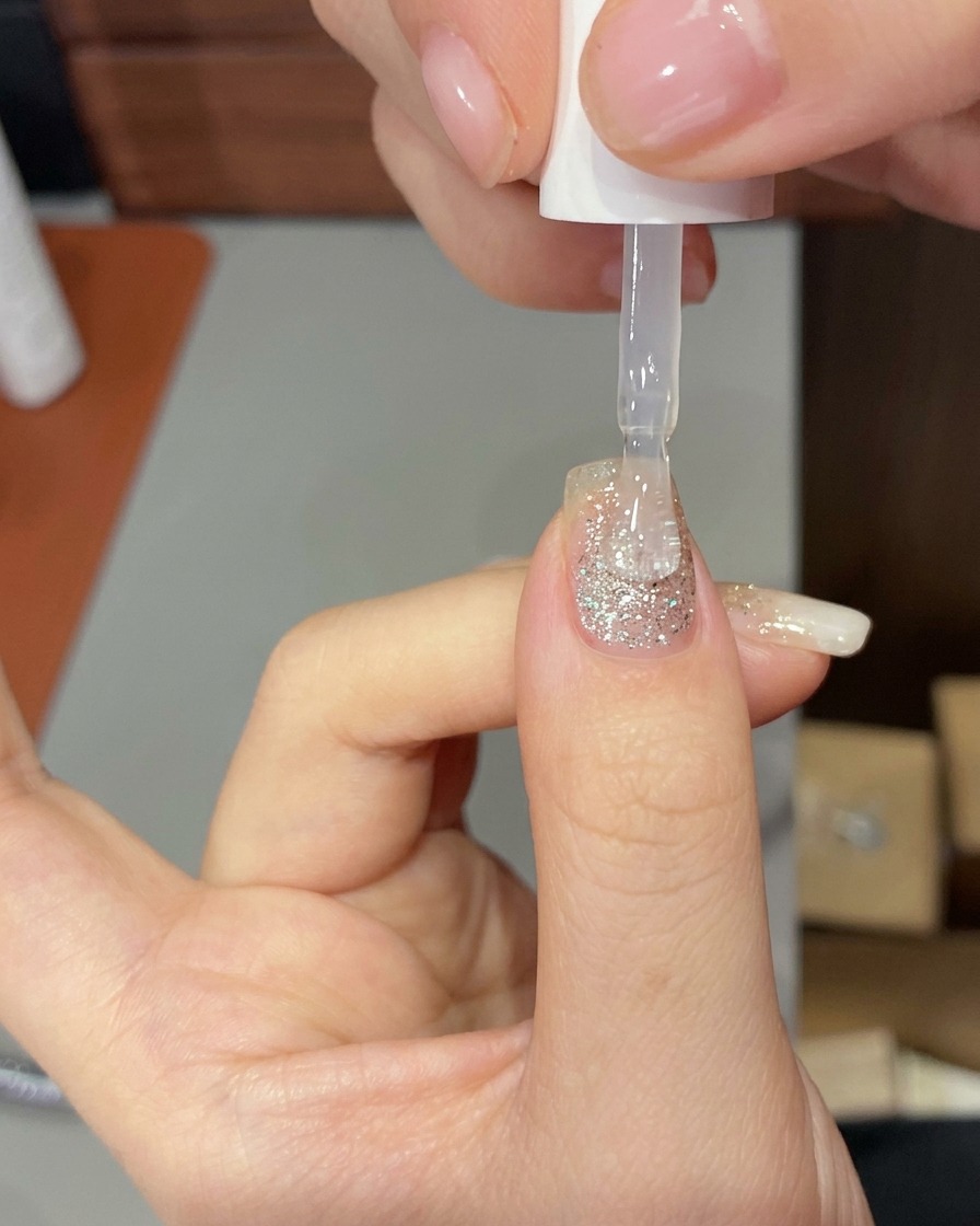 Une main placée à lintérieur dune lampe UV/LED professionnelle, les ongles illuminés par la lumière de catalyse.