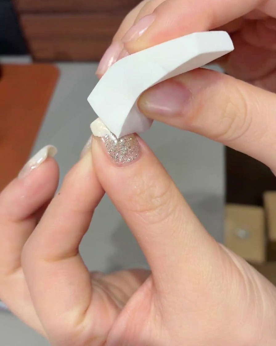 Gros plan dune éponge à maquillage tapotant du gel blanc laiteux sur la pointe dun ongle pour former un dégradé doux.